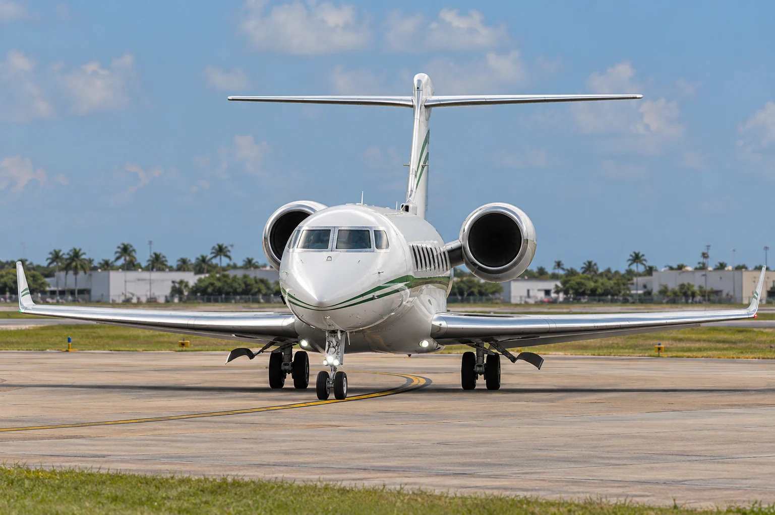 White business jet with green stripes, full wingspan visible on a South Florida airport taxiway